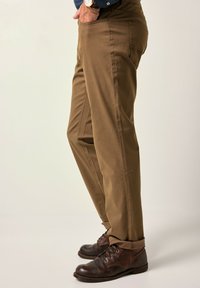 Hnědé bavlněné kalhoty se rovnýcm střihem, s bočními kapsami a hladkým povrchem. Spárovány s tmavě hnědými koženými botami.