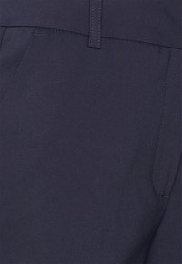 Marinblå byxor med slät yta, med sidofickor och kontrasterande sömmar längs midjan för extra detaljer.