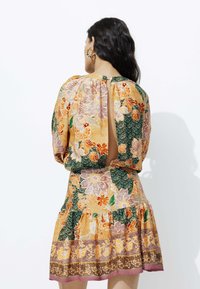 Robe florale multicolore avec manches bouffantes, dos ouvert et ourlet à volants. Présente des motifs orange, vert et violet avec des accents vintage.