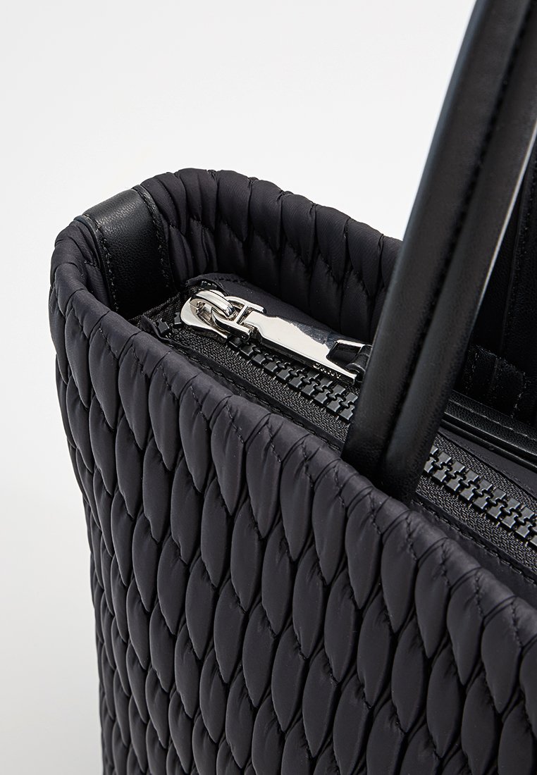 Schwarze gestepptes Handtasche mit strukturierter Oberfläche und glatten Lederakzenten, mit einem silbernen Reißverschluss und langen Tragriemen für einfaches Tragen.