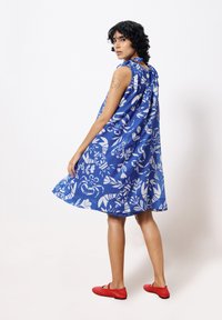 Blaues Blumenkleid mit weißen Mustern, ärmelloses Design und gebundenem Ausschnitt. Kombiniert mit roten Ballerinas, die eine einfache, glatte Textur aufweisen.