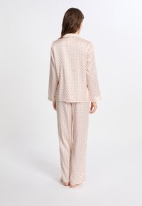 Conjunto de pijama rosa claro con lunares rojos, de mangas largas y pantalones, tejido suave, corte relajado, parte superior con botones y detalles en el cuello.