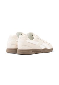 Baskets en daim blanc avec des accents en cuir lisse, un bout arrondi et une semelle en caoutchouc marron à rainures, avec un logo sur le talon.