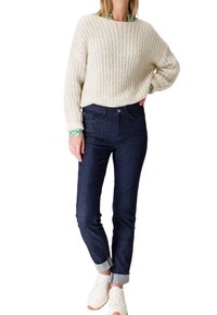 Suéter de punto crema con un ajuste holgado, combinado con unos jeans de denim azul oscuro con los puños doblados y zapatillas blancas.