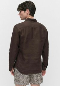 Chemise en lin marron à manches longues avec un col boutonné, coupe décontractée et texture légère. Portée avec un short à motif en losange.