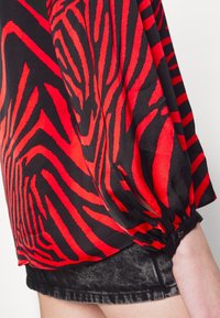 Blouse à manches longues rayée zèbre rouge et noire avec poignet boutonné portée avec un short en denim noir.