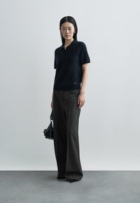 Black fuzzy short-sleeve polo shirt paired with dark pinstriped wide-leg trousers; model carries a small black handbag.