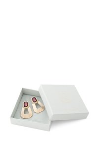 Gouden oorbellen met een geometrisch ontwerp, featuring een dieproze octagonale steen en gelaagde lijnen, gepresenteerd in een lichtgrijze doos.