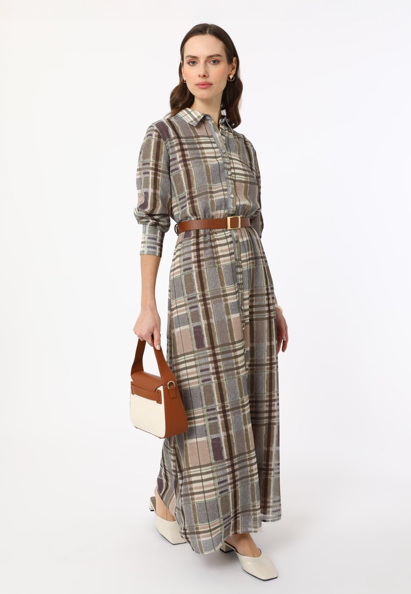 Maxi dress in plaid pattern featuring long sleeves, a belted waist, and button-down front. Accompanied by a brown and cream handbag.