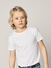 T-shirt en coton blanc à manches courtes, col rond simple, porté par un enfant aux cheveux blonds clairs et à l'expression neutre.