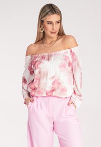 Bluzka z odkrytymi ramionami w różowy kwiatowy wzór na białym tle, połączona z jasnoróżowymi spodniami. Miękki, lekki materiał.