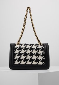 Black and white houndstooth-patterned handbag with a black leather base and a gold chain strap, featuring a rectangular shape and clasp closure.