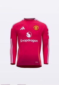 Červený dres s dlhým rukávom a bielymi pruhmi na ramenách, s logom Manchester United, značkou "Snapdragon" a materiálom odvádzajúcim pot.