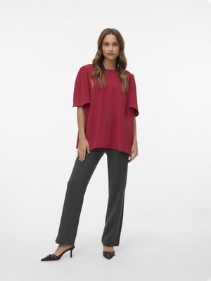Red textured top with short puff sleeves, paired with dark green tailored pants and brown pointed-toe heels with decorative accents.