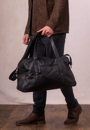 Black leather duffel bag with two top handles, a detachable shoulder strap, and subtle stitching details. Features front zip pocket.