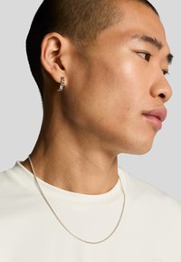 Sølv hoops ørering med et tekstureret design og en tynd, poleret sølv kæden halskæde. Båret af en person i en enkel hvid skjorte.