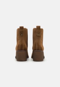 Stivali ankle in suede marrone con tacco a blocco, dotati di una linguetta sul retro per un facile indossamento e dettagli di cucitura sottili sui lati.