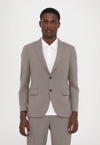 Hellgraue Anzugjacke mit schmaler Passform, ausgestattet mit zwei Knöpfen, Reverskragen und Fronttaschen. getragen über einem weißen Hemd mit Kragen.