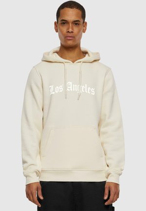Sudadera color crema hecha de una tela suave con un bolsillo tipo canguro. Presenta el texto "Los Ángeles" en blanco en un tipo de letra en negrita. Puños y dobladillo elásticos.
