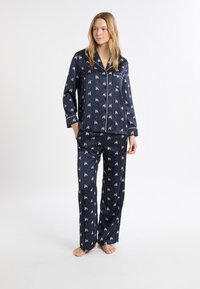 Granatowy satynowy komplet piżamowy z powtarzającym się nadrukiem małych postaci, koszula na guziki z kieszenią i spodnie o luźnym kroju.