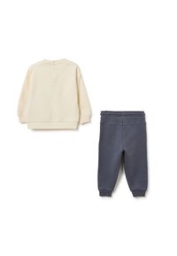 Helles beiges Sweatshirt mit rundem Halsausschnitt und Knopfverschluss hinten, kombiniert mit dunkelblauen Sweatpants mit elastischem Bund.