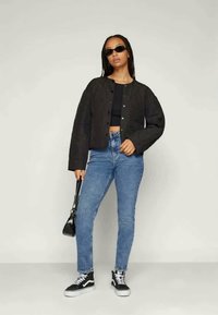 Μαύρο κομμένο τζάκετ με κουμπιά στο μπροστινό μέρος, συνδυασμένο με ψηλόμεσα μπλε τζιν και μαύρα sneakers Vans. Τα αξεσουάρ περιλαμβάνουν μικρά γυαλιά ηλίου και μια τσάντα.