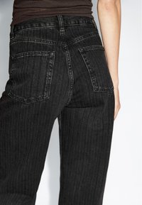 Black pinstriped high-waisted jeans with a straight leg cut. Features two back pockets, visible stitching, and a textured denim finish.