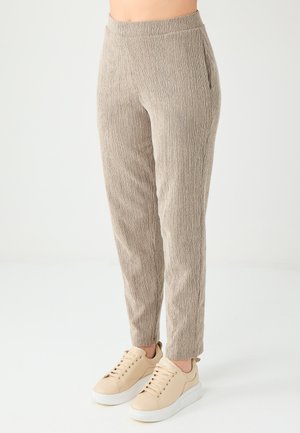 Pantalons taper beige texturé avec une taille élastique et des poches latérales, associés à des baskets beige clair sur fond blanc.