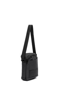 Kompaktne must õlakott reguleeritava rihmaga, esitasku ja tõmblukuga põhiosaga, seisab püsti valgel taustal.