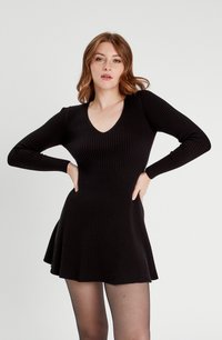 Czarna, prążkowana sukienka z długim rękawem, o dopasowanej gumce i rozkloszowanej spódnicy. Posiada dekolt w kształcie litery V i gładką fakturę.