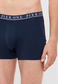 Sötétkék boxer alsónadrág, puha, rugalmas anyagból készült. Jellemzője egy elasztikus derékpánt, fehér betűkkel "PIER ONE" logóval.