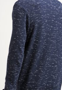Pull en maille texturée bleu marine avec un motif marbré, doté d'un col rond et de manches longues. Le tissu paraît tricoté et léger.
