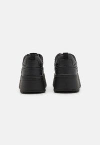 Black sneakers featuring a textured leather upper, cushioned collar, and thick rubber sole for added height; includes pull tabs at the heel.