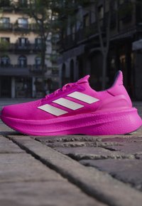Lys pink sportssko med hvide striber på en brostensbelagt gade i en urban setting om dagen.