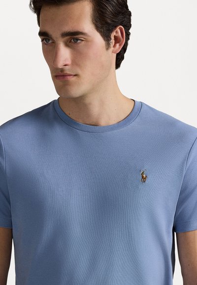 Hele sinine puuvillane lühikeste varrukatega T-särk, millel on ümmargune kaelus ja vasakul rinnal tikitud logo ratsaniku kujutisega.