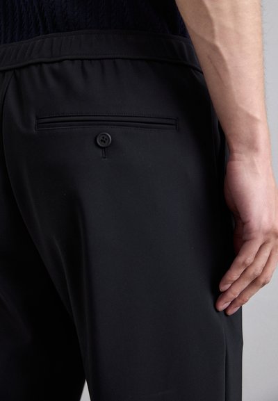 Schwarze Hose mit einem glatten, elastischen Bund und einer Gesäßtasche mit Knopfverschluss. Der Stoff wirkt leicht und flexibel.