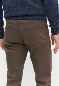 Bruna bomullsbyxor med rak passform, som har två bakfickor och diskreta sömnadsdetaljer, kombinerat med en marinblå strukturerad tröja.