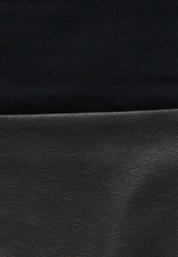 Κοντινή λήψη μαύρου ριγωτού υφάσματος πάνω από λείο μαύρο δέρμα, που αναδεικνύει τις αντίθετες υφές και υλικά.