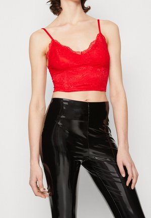 Rød blonder bralette med en bølget halsudskæring og justerbare stropper, kombineret med højglans sorte leggings. Teksturkontraster mellem materialerne.