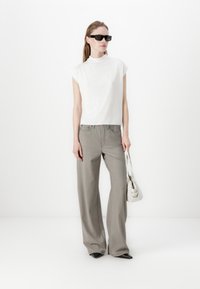 Top corto ajustado blanco de manga corta combinado con pantalones grises de pierna ancha de tiro alto. Los accesorios incluyen gafas de sol negras y un bolso blanco.