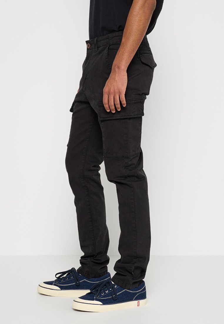 Pantalones cargo negros de algodón, con bolsillos laterales, un ajuste recto y una textura mate elegante. Combinados con zapatillas de deporte azul marino.