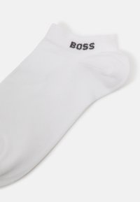 Chaussettes blanches jusqu'aux chevilles en mélange de coton, avec une texture côtelée et le logo noir "BOSS" près de l'ourlet. Aucun autre motif ou accent.