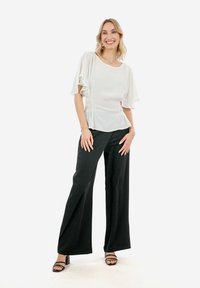 Blusa bianca a maniche corte con lati arricciati, abbinata a pantaloni neri a gamba larga. Tessuto liscio e vestibilità comoda; scollatura aperta.