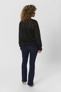 Schwarzes Spitzenoberteil mit strukturiertem Muster, langen Ärmeln und elastischem Saum, kombiniert mit dunkelblauen Schlagjeans und beigen High Heels.