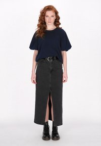 Maglietta cropped blu navy con maniche a sbuffo abbinata a una gonna maxi in denim nera con spacco frontale, completata da stivali neri con lacci.