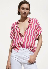 Short-sleeve shirt featuring a pink, white, and orange wave pattern, made of lightweight fabric, paired with white high-waisted jeans.