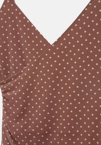 Braunes Stoffoberteil mit weißen Polka-Punkten, das ein Überkreuz-Design und geraffte Details auf einer Seite aufweist. Glatte Textur, lässiger Stil.