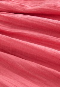 Rosa texturerad tyg med en mjuk, lätt känsla, som visar subtila veck och ett slätt, något oregelbundet mönster.