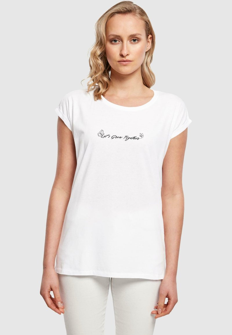 Hvid bomulds T-shirt med rullede korte ærmer, rund halsudskæring og sort broderet tekst "Lad os vokse sammen," med sommerfugle detaljer.