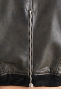 Czarna skórzana kurtka bomber z metalowym zamkiem błyskawicznym biegnącym wzdłuż środka; posiada dzianinowe ściągacze na mankietach i u dołu, zapewniające dopasowany wygląd.